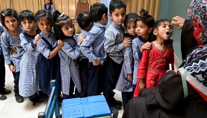 A health worker administers polio drops to school children for vaccination during a door-to-door poliovirus eradication campaign in Lahore on April 21, 2025. — AFP