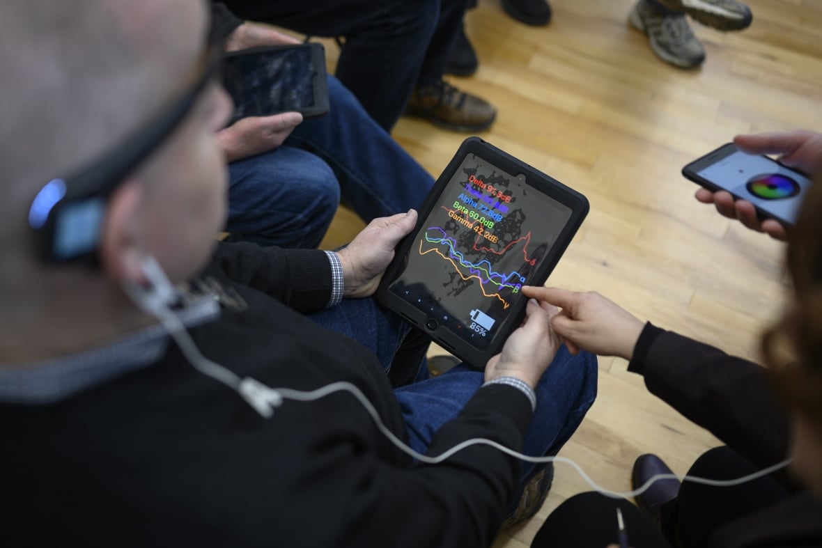 A man is seated, holding an electronic device in his hands