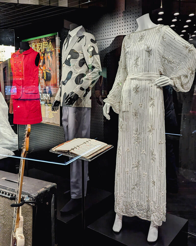 Three stage costumes from Australian music artists including a long white dress, black and white shirt and red mini dress