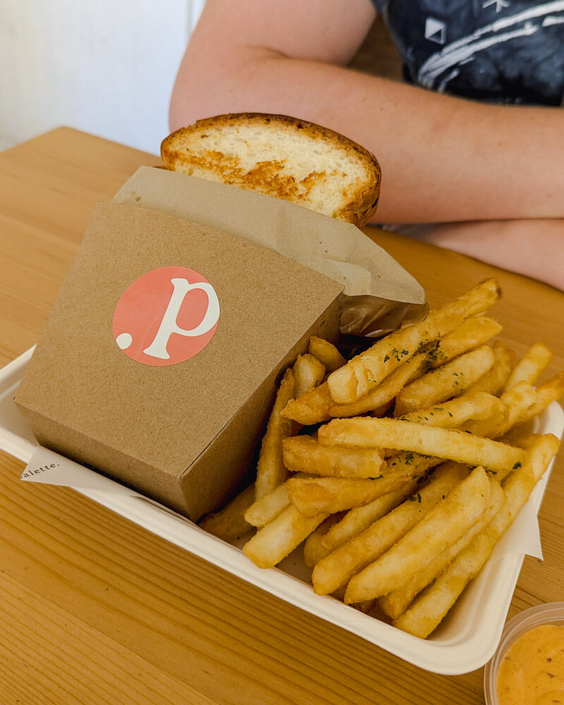 Brioche sandwich in brown cardboard sleeve served with chips at Palette. in Melbourne