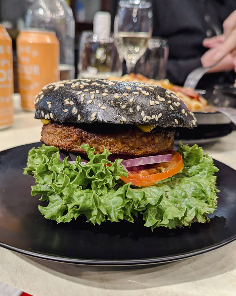 Burger served in a black sesame bun with lettuce and tomato at Wonky Trolley