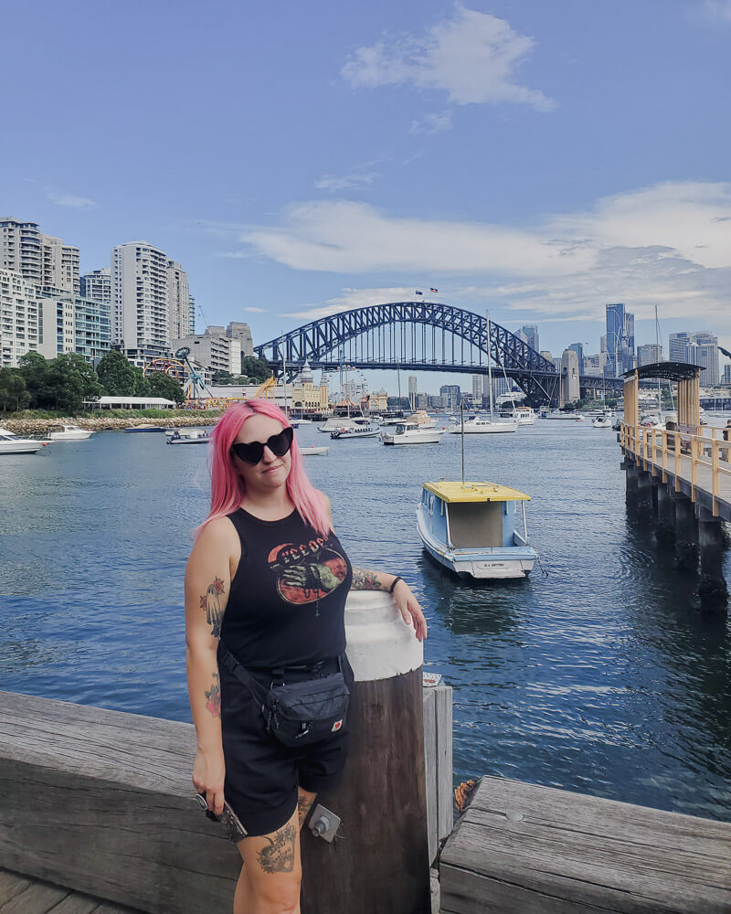 Milly is stood in front of a harbour with boats, with Sydney Harbour in the background